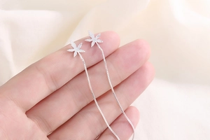 Detailed macro view of silver maple leaf earrings with delicate long tassel chains