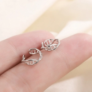 Close-up of a silver DNA double helix ear cuff held on a fingertip for size reference