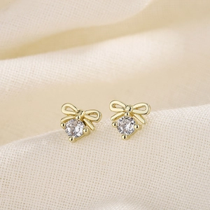 Elegant gold bow earrings with sparkling round zircon studs on textured fabric