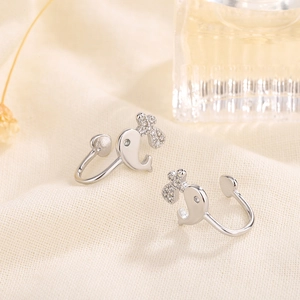 Elegant silver dolphin ear cuffs with sparkling bow detail on a warm textured background