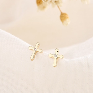 Élégantes boucles d'oreilles croix dorées avec zircon central sur tissu blanc doux