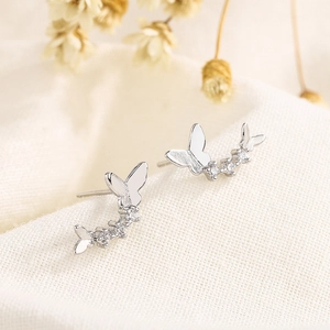 Minimalist silver butterfly stud earrings with sparkling cubic zirconia on textured fabric