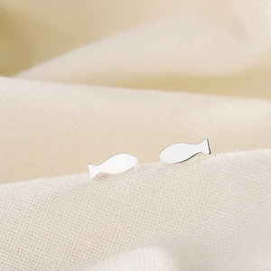 Boucles d'oreilles poisson en argent minimalistes sur une surface en tissu beige