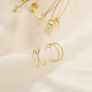 Minimalist gold U-shaped and cross X ear cuffs set displayed on beige textured linen