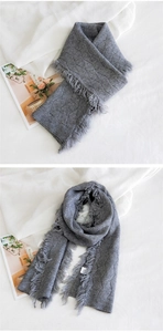 Détail d'une écharpe en tricot gris montrant la texture losange et les franges