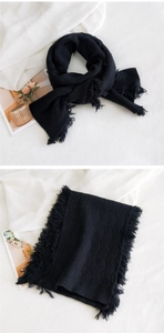 Détail d'une écharpe en maille noire avec motif losange, franges élégantes et texture épaisse