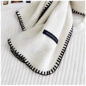 Detail of cream knit scarf featuring black contrast stitching and a decorative fabric tag