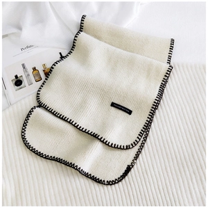 Detail of white knit scarf with black stitched edges and decorative text patch