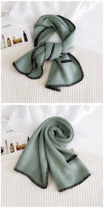 Macro detail of sage green knit scarf featuring black stitched edges and woven tag