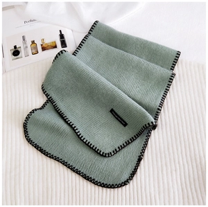Detail of knitted scarf in Morandi green with black contrast stitching and textile label
