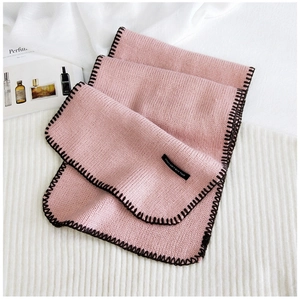 Detail of pink knitted scarf with black whip-stitch edges and white logo label tag