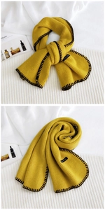Detail of ginger yellow knitted scarf with black hand-stitched edges and textured weave