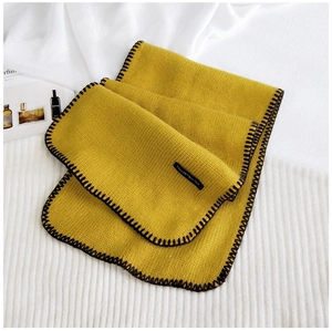 Close-up of ginger yellow chunky knit scarf with black edge stitching and text label