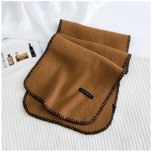 Detail of chunky knit brown scarf featuring black whipstitch edges and a woven text label