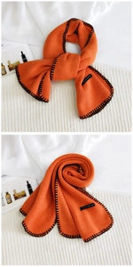 Detail of bright orange knit scarf with black contrast stitching and graphic label tag