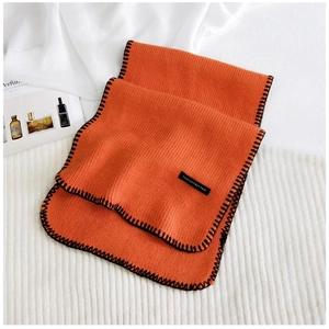 Close-up of orange ribbed knit scarf featuring black contrast edge and woven slogan patch