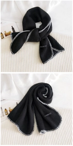 Detail of black knit scarf with white stitched edges and decorative logo patch
