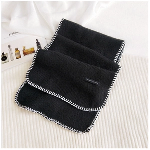 Detail of black knit scarf featuring white stitched edges and decorative text patch