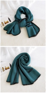 Macro detail of dark green knit scarf featuring contrasting black stitched edges and label