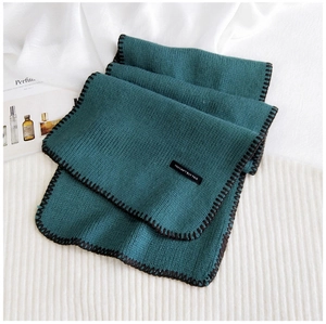 Detail of dark green knit scarf featuring black stitched edges and a minimalist woven label