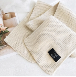 Close-up of beige knitted scarf with vertical stripe texture and black fabric brand label