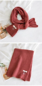 Détail macro de l'écharpe en maille rouge avec côtes haute densité et étiquette de marque