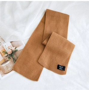 Close-up of caramel knitted scarf with ribbed texture and black fabric logo label