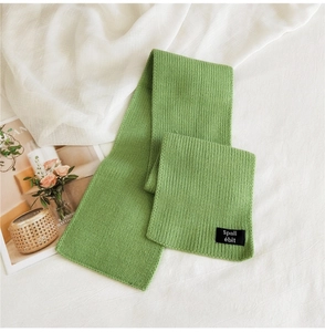 Close-up of green rib-knit scarf detail with woven brand label on soft fabric