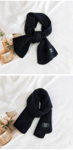 Detail view of black knit cross-over scarf with ribbed texture and woven brand label