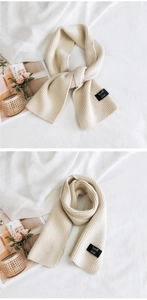 Detail of beige ribbed knit scarf with woven brand label shown in cozy lifestyle setting