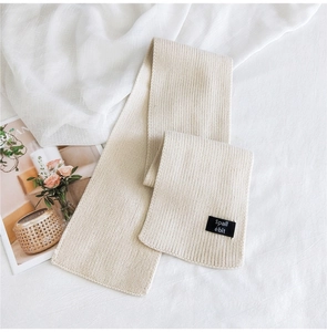 Detail of beige knit scarf with ribbed texture and black woven brand label
