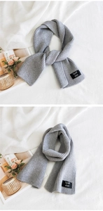 Detail of grey ribbed knit scarf with a square black brand label and soft wool texture
