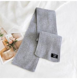 Detail of gray knitted scarf with black fabric label on soft white textured background