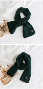 Detail of dark green ribbed knit scarf with cross-through buckle and woven label