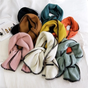 Multi-colored knitted scarves with black blanket stitch edges and decorative woven labels