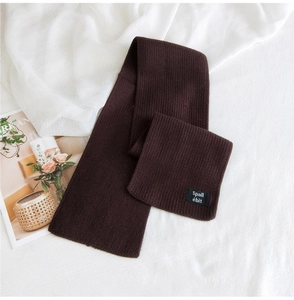 Detail of coffee brown ribbed knit scarf with square brand label on textured cloth