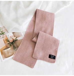 Detail of pink ribbed knit scarf with woven brand label on white fabric background