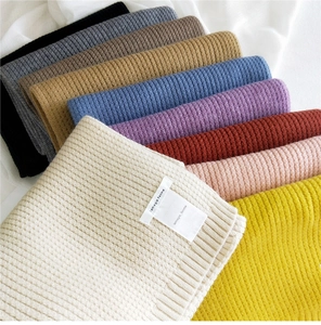 Detailed macro view of multi-color ribbed knit scarves showing thick wool texture and labels