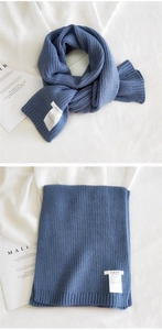 Detailed view of dark blue chunky knit scarf featuring a white brand label on soft fabric