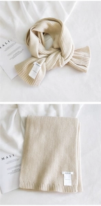 Detail of beige chunky knit scarf with vertical rib pattern and brand label