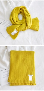 Detail of bright yellow chunky knit scarf with white brand label on fabric background