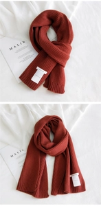 Detail of brick red ribbed knit scarf showing clear texture and white brand label