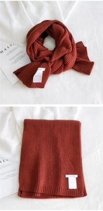 Detailed macro view of the thick rust-red knitted texture and ribbed hem on the scarf