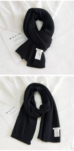 Detail of rib-knit black scarf showing soft cashmere texture and minimalist woven label