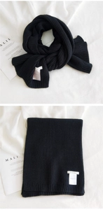 Close-up of black ribbed knit scarf with a white brand label on minimalist background