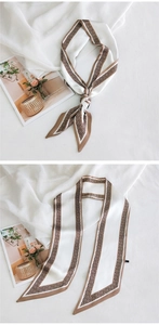 Détail d'un long foulard en soie blanc avec motifs de losanges bruns utilisé comme bandeau