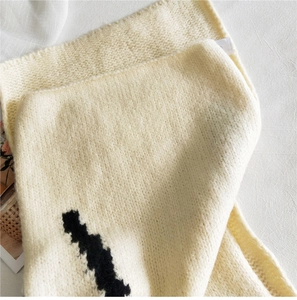 Close-up of cream knitted scarf with thick texture and abstract black pattern print