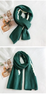 Detailed view of dark green knitted scarf featuring white abstract pattern and thick texture