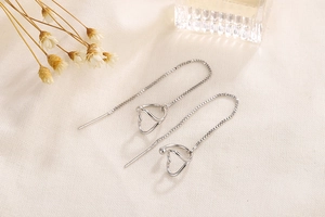 Detail of silver long tassel threader earrings with geometric heart shape on fabric
