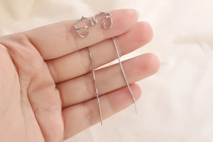 Detail of silver heart tassel ear line earrings held by hand showing delicate chain